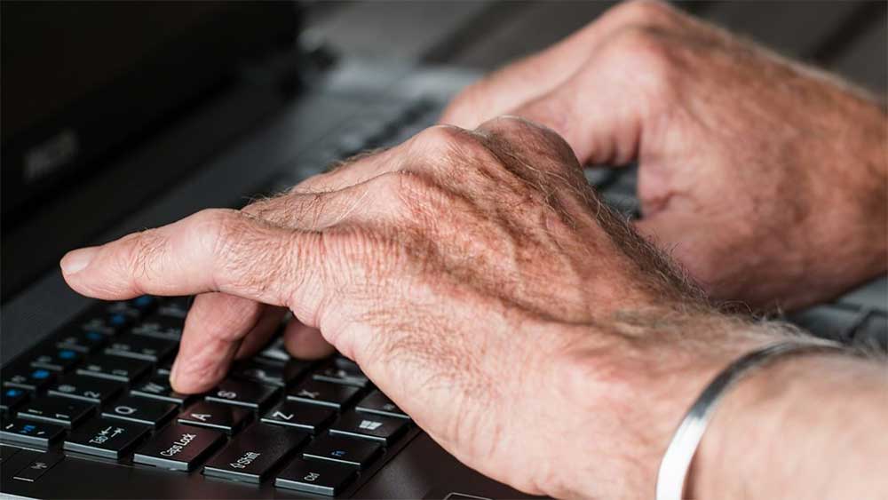 senior hands on laptop keyboard
