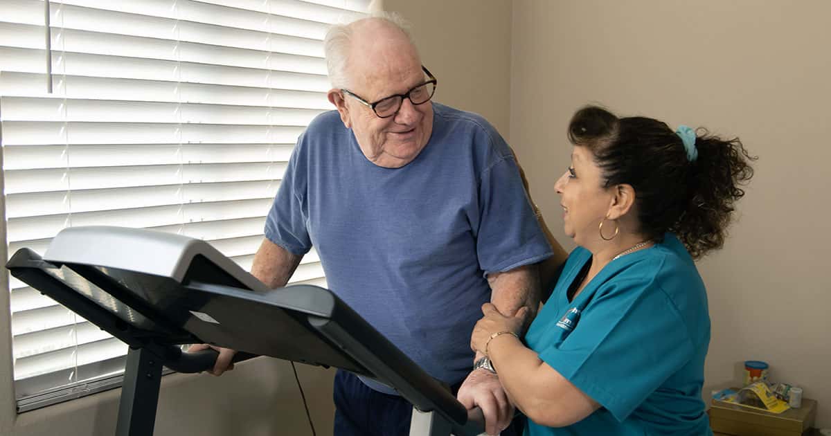 caregiver helping senior walk on treadmill