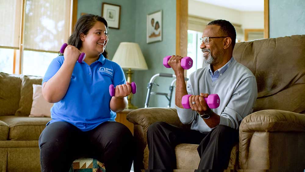 caregiver and senior lifting hand weights while seated