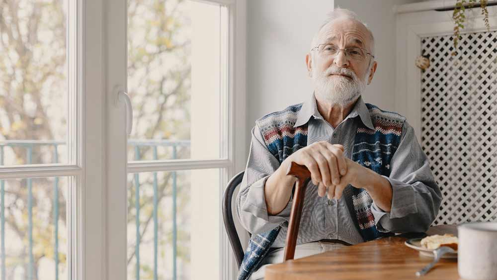 senior-man-with-cane-sitting-near-window