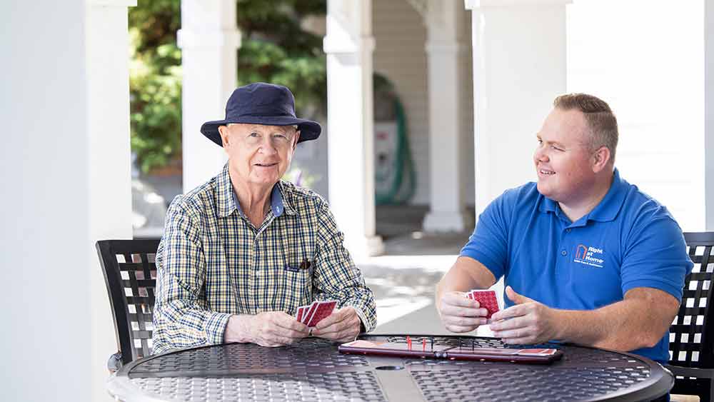 senior male and caregiver playing cards