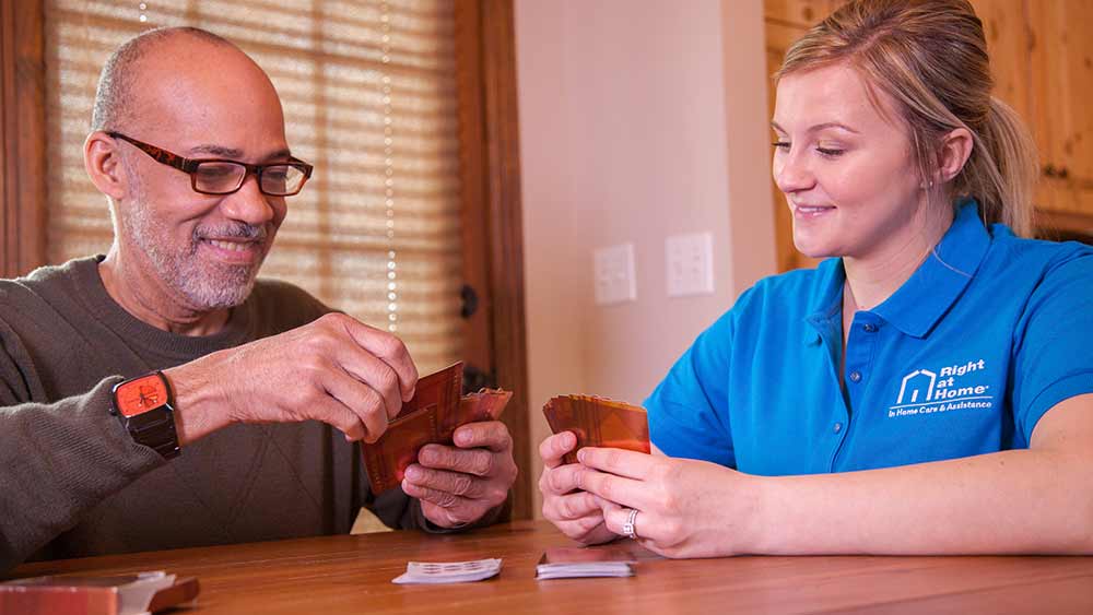 senior playing cards at table with caregiver