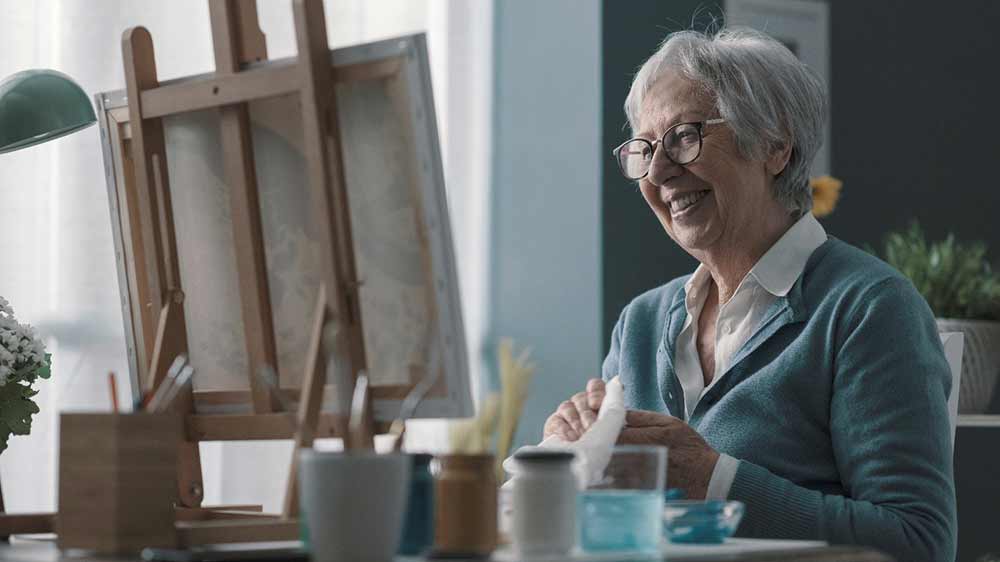 senior-woman-sitting-at-easel-painting