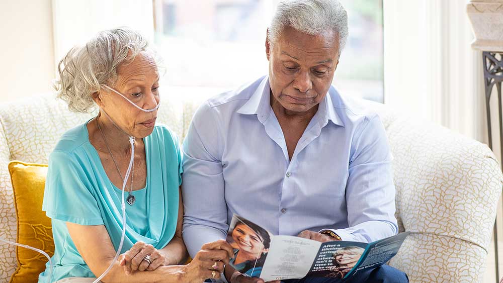 senior woman with oxygen and senior man sitting on couch reading brochure