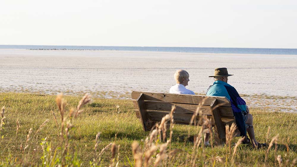 senior-couple-sitting-on-bench-near-ocean