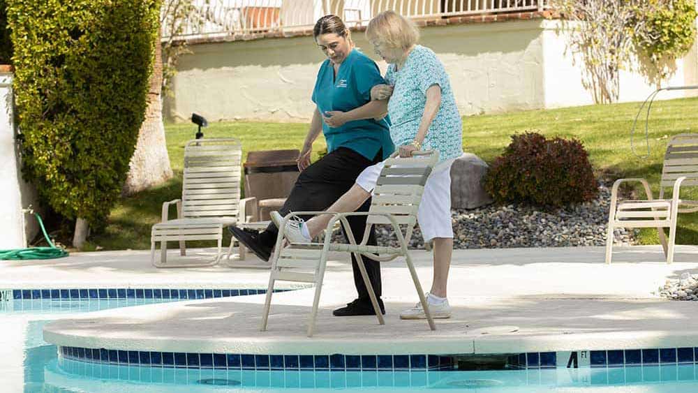 Caregiver exercising with senior by swimming pool