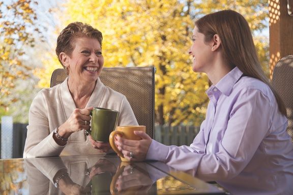 Caregiver and Senior Enjoying a Beverage Together While Seated Outside at Table Surrounded by Fall Trees 