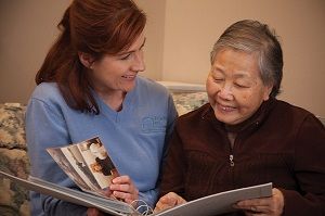 Right at Home Caregiver Looking at Photo Album with Senior Woman at Home