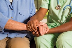 Person in Green Scrubs Wearing Stethoscope Holding Hands with Elderly Person in Blue Shirt