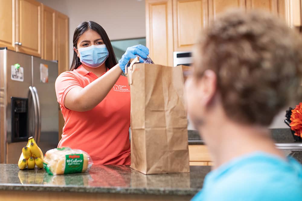 caregiver wearing PPE unpacking groceries for senior adult