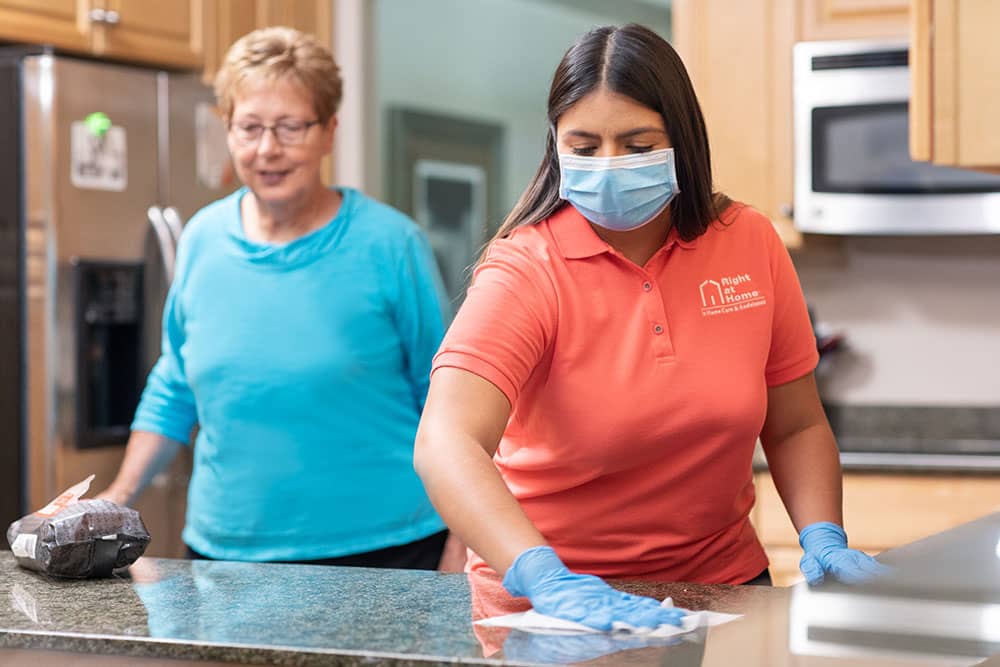 caregiver wearing PPE wiping counters for senior adult