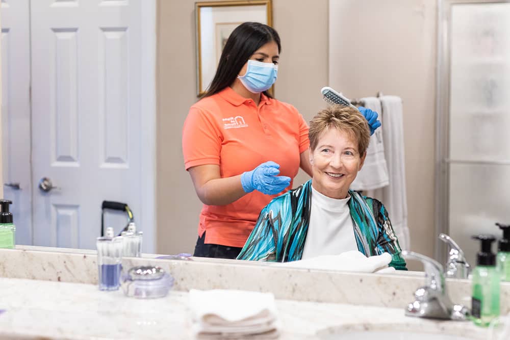 caregiver wearing PPE brushing the hair of senior adult