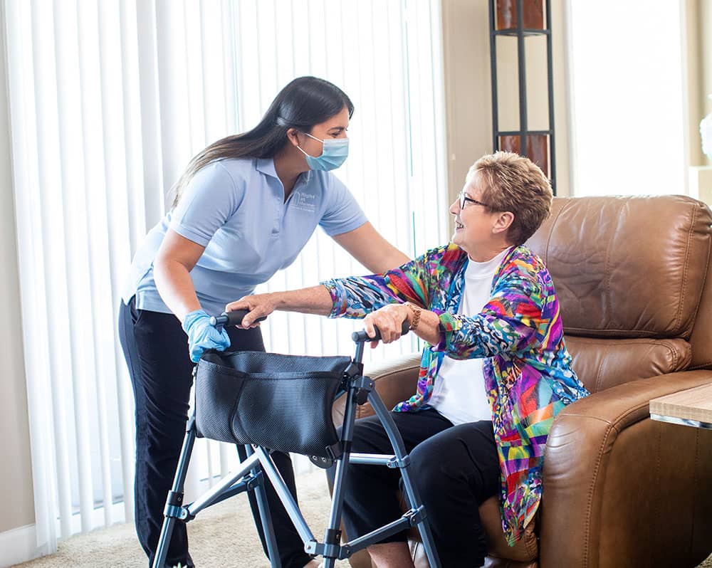 caregiver wearing PPE assisting senior adult with standing using a walker