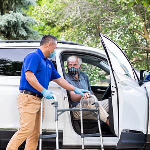 Caregiver wearing PPE assisting senior client out of the car