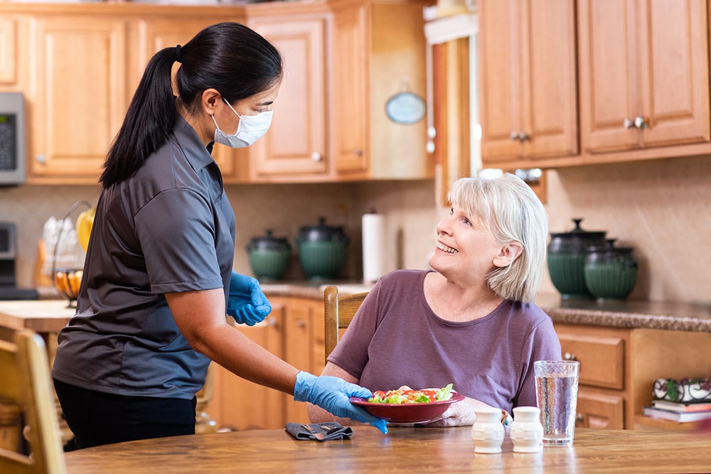 Caregiver wearing PPE serving senior client a meal