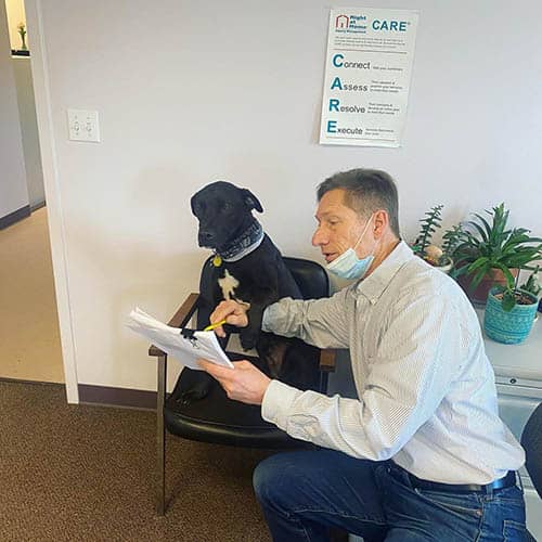 Right at home of boston metro west's Bob kneeling down showing a flyer to Hank the dog sitting on a chair in the office