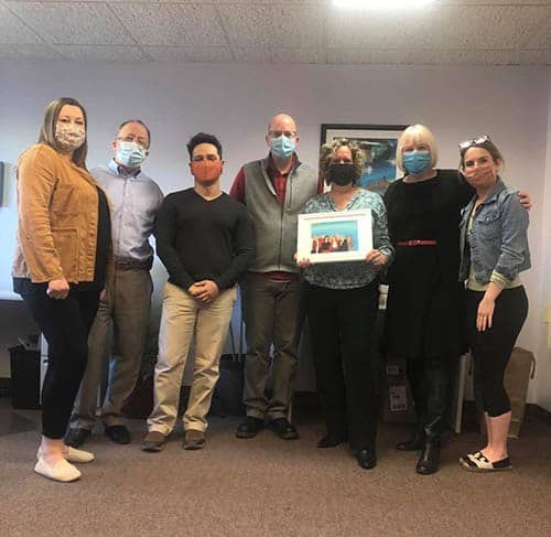 The office staff of Right at Home Boston Metro West posing with a painting created by Max