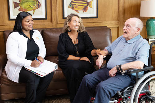 Two Women on a Couch Discussing Care with a Senior Man in a Wheelchair