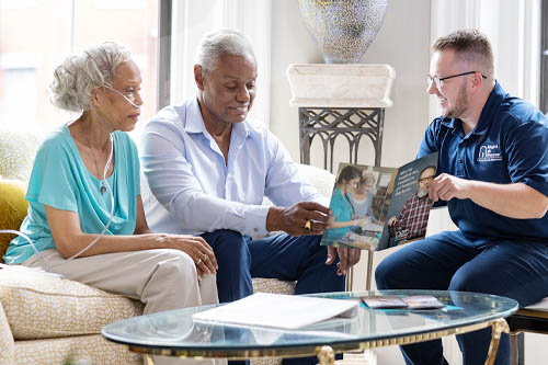 Senior African American Couple Sitting on a Couch Reviewing Care Support with a Franchise Owner Sitting in a Chair Beside Them