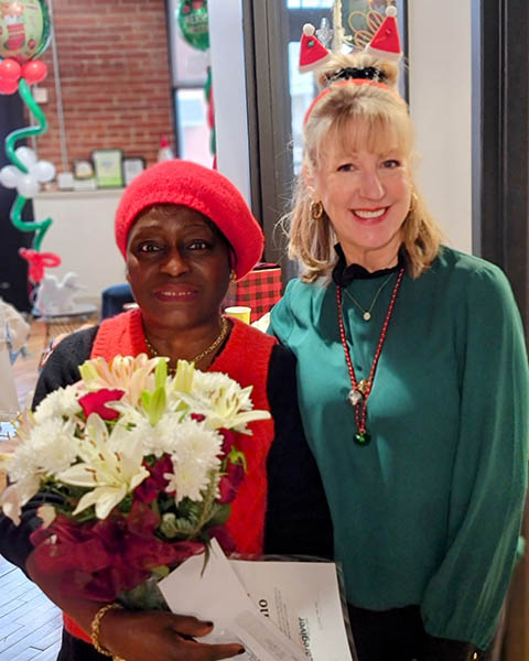 Caregiver of the Year Monica holds flowers and stands next to Owner, Carole Luber.