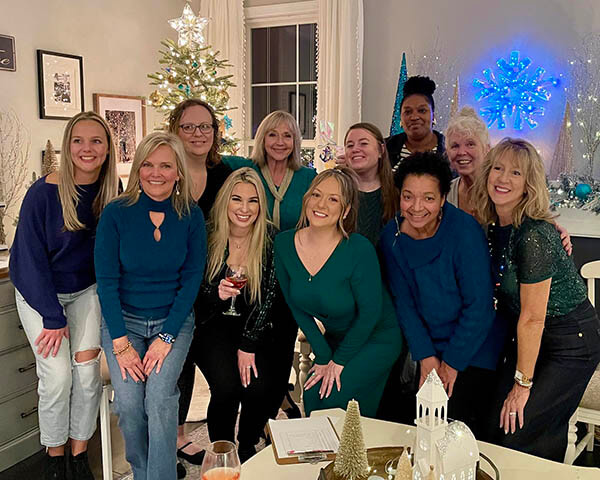 Several females standing in a living room with a Christmas tree in the background.