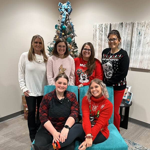 The Carroll County office staff, 6 females, pose in front of a Christmas tree.