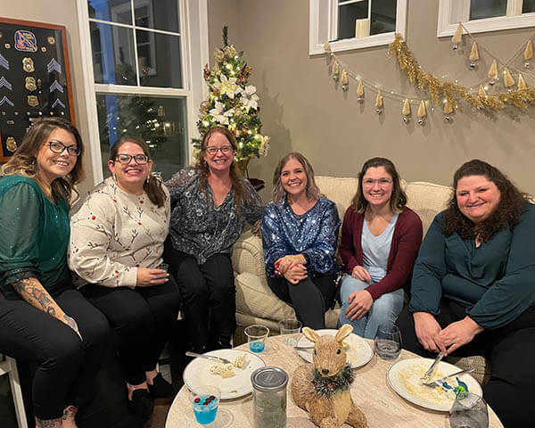 Six females sitting around a coffee table with holiday decorations in the background.