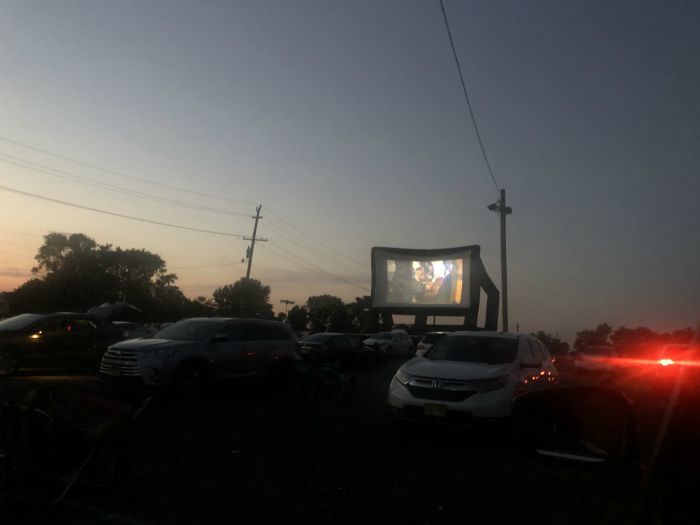 a photo of the large screen that the movie is playing on from a distance with cars in the forefront 