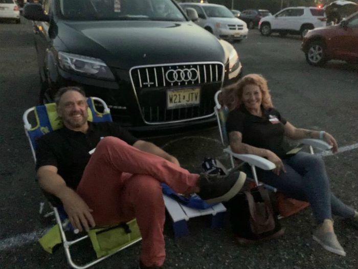 two people, one male, one female, sitting in lawn chairs to watch the movie outside of their car