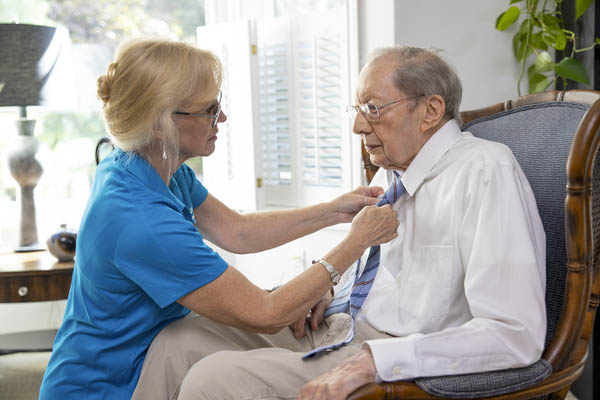 Caregiver tying an elderly man's tie