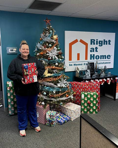 Amber stands next to a Christmas tree holding a gift.