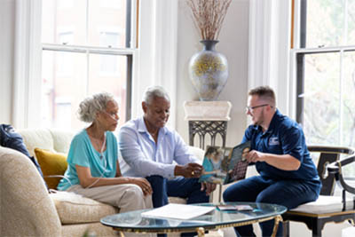 Three individuals engaged in a discussion in a bright living room, seated around a coffee table.