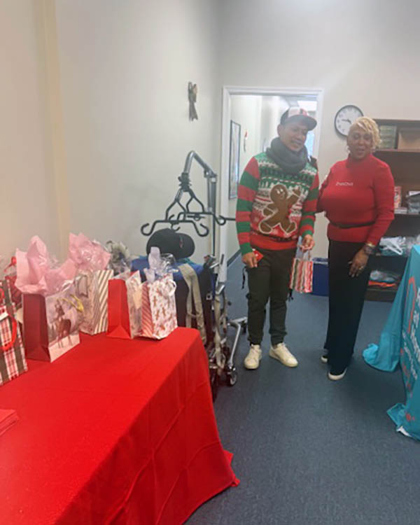 Gloria stands with a caregiver next to a table of gifts.