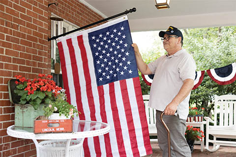 Senior male standing on porch admiring the American flag