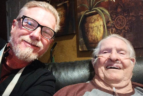 Male Caregiver Sitting Beside His Senior Male Client Both Facing the Camera