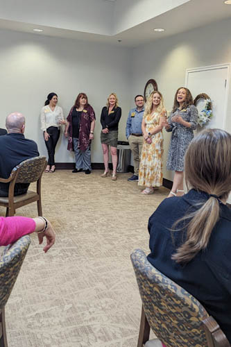 Group of presenters stand in a corner of the room talking to an audience sitting at tables.