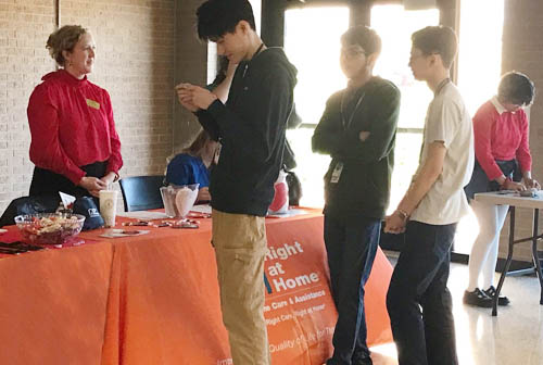 Female Right at Home Staff Member Sitting at a Job Fair Display Table with a Crowd of People at the Table