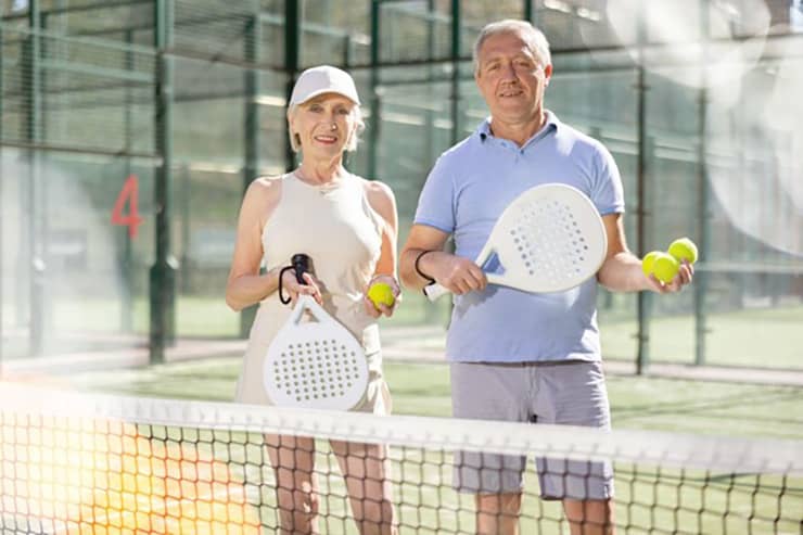 an elderly man and woman hold pickleball rackets on a court