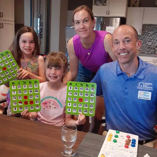 Right at Home Northern Kansas City Staff and Family Posing Together Facing the Camera Holding Bingo Cards