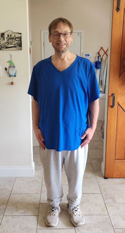 Bill Nash, caregiver, standing straight in a baggy blue shirt