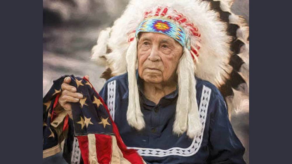 Senior Native American veteran Choc Charleston posing in formal headdress and holding a flag