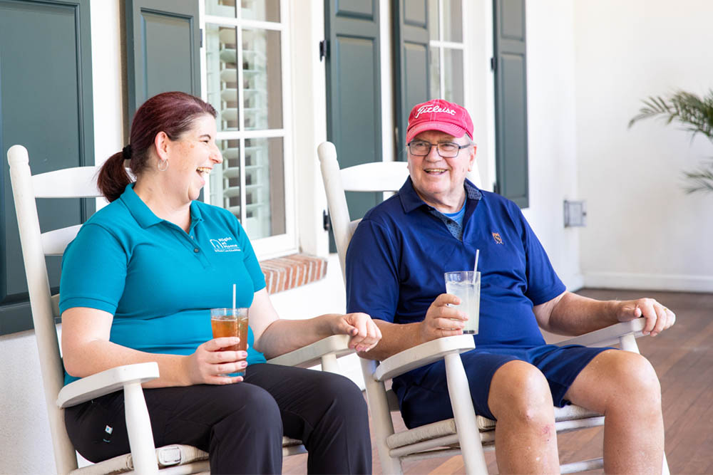 Female Caregiver with Senior Male Client Sitting on the Porch Laughing