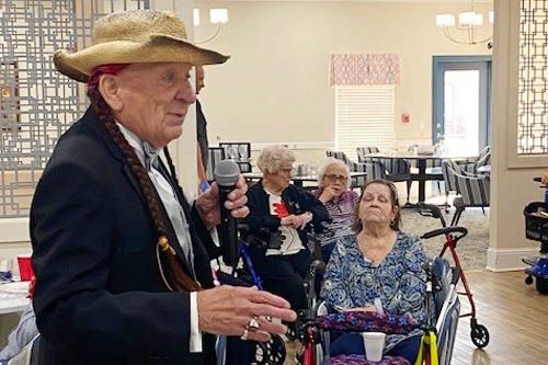 Elderly man in a cowboy hat speaks to an audience prior to singing at the event.