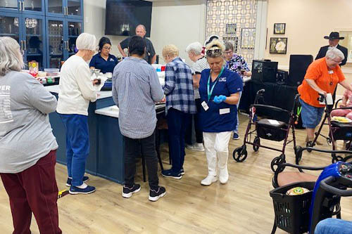 A crowd of seniors and caregivers standing around a buffet food table at the event.