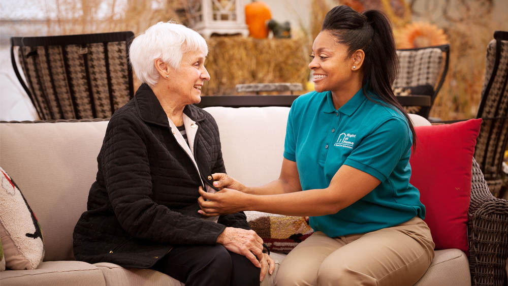 Female Caregiver Buttoning the Jacket of a Female Client with Dementia