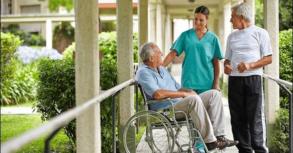 senior-man-in-wheelchair-talking-to-female-caregiver-and-senior-male-outside