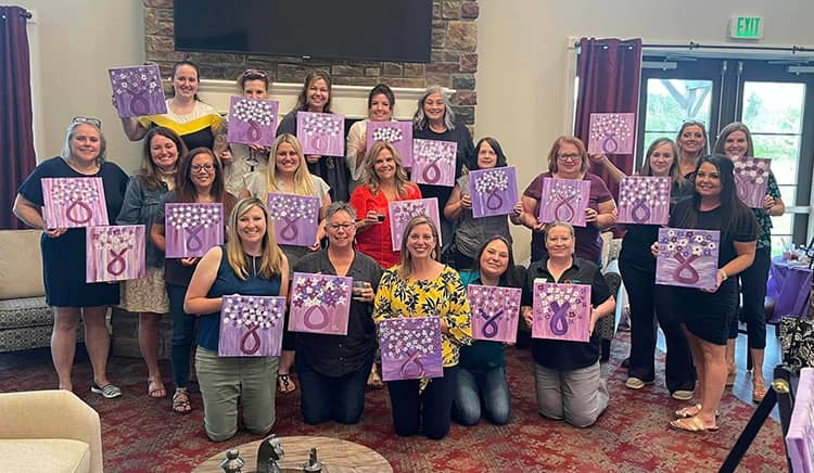 A group of participants in the pinot and paint for Alzheimer's stand with their paintings 