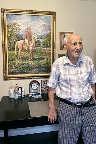 Senior Male Client Standing Next To One of His Paintings