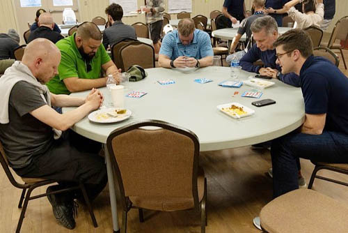 Veterans join in prayer seated around a round dinner table at Camp Hope