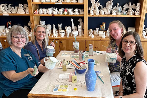 Group of women smiling at the camera sitting at a table working on painting pottery